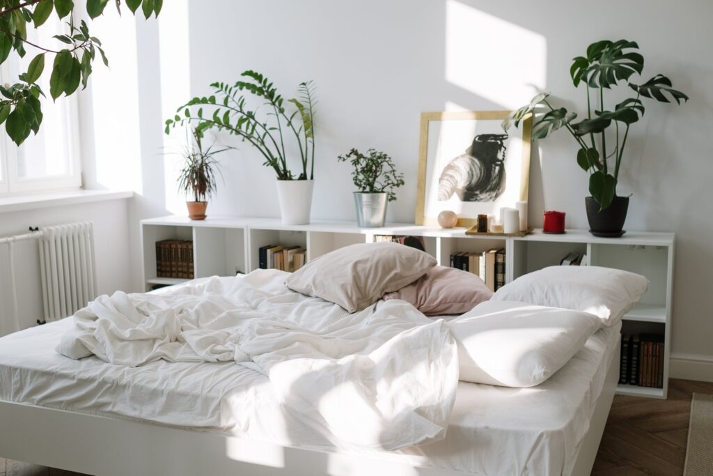 Ungemachtes Bett mit weißem Regal im HIntergrund und Pflanzen